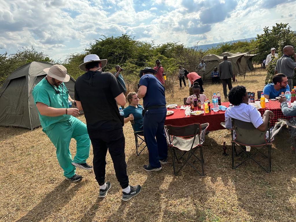 Volunteers sharing lunch around a red-clothed table beside tents at a field camp