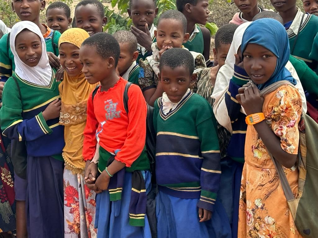 A crowd of smiling schoolchildren in green uniforms and colourful headscarves