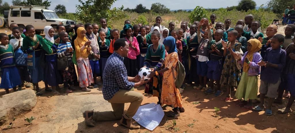 A volunteer kneels with a football in front of a crowd of excited schoolchildren